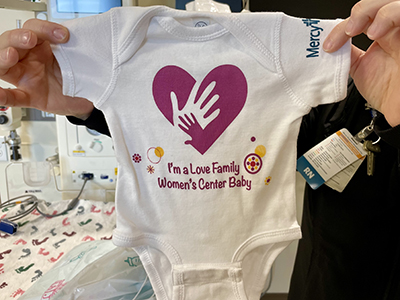 A onesie that says "I'm a Love Family Women's Center Baby" for Mercy.
