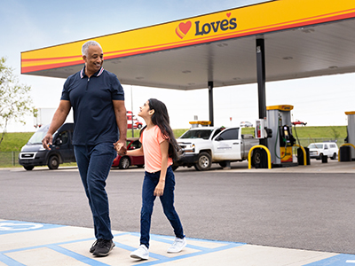 Two people walking in front of Love's Travel Stops gas pumps.
